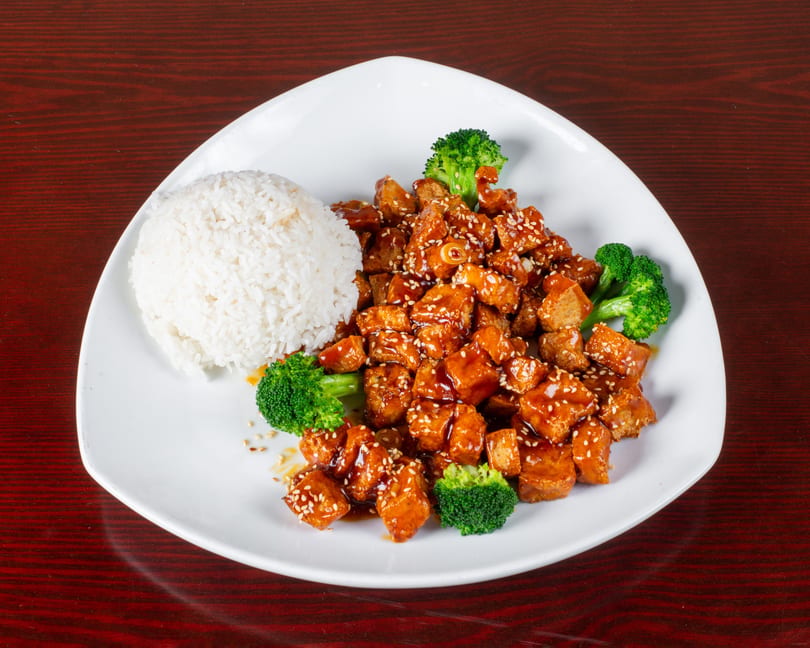 Sweet and sour chicken with white rice and broccoli florets on a white plate.