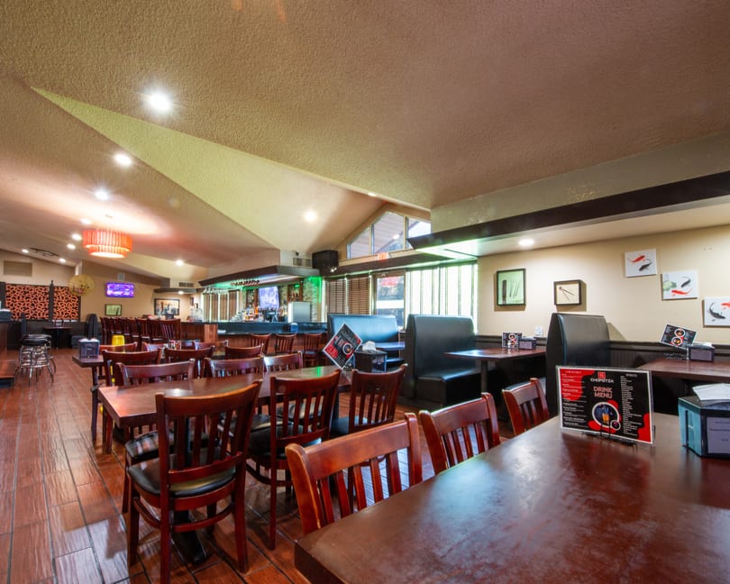 Interior view of a restaurant with wooden tables, chairs, booths, and a bar area.