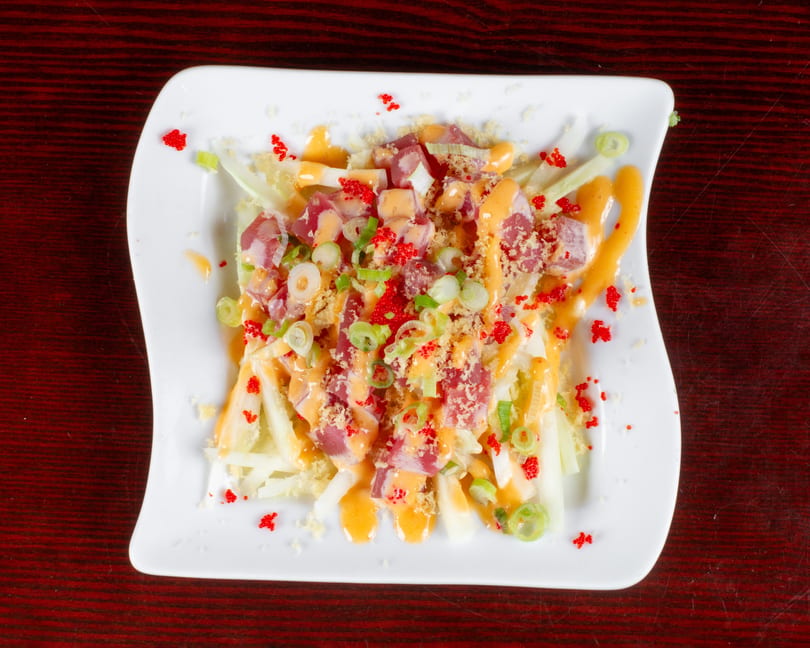 A vibrant poke salad with tuna, green onions, and orange sauce, topped with red roe on a white plate.