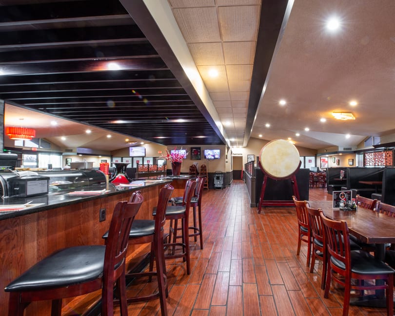 Interior view of a restaurant with a sushi bar, dining tables, and a large drum.