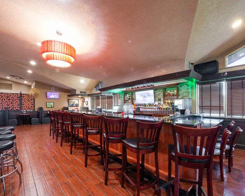A well-lit bar area with wooden bar stools, a fully stocked bar, and booth seating in the background.