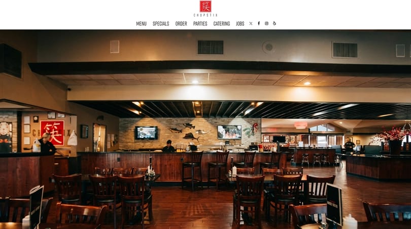 Spacious Chopstix restaurant interior with dark wood tables, chairs, and a long sushi bar.