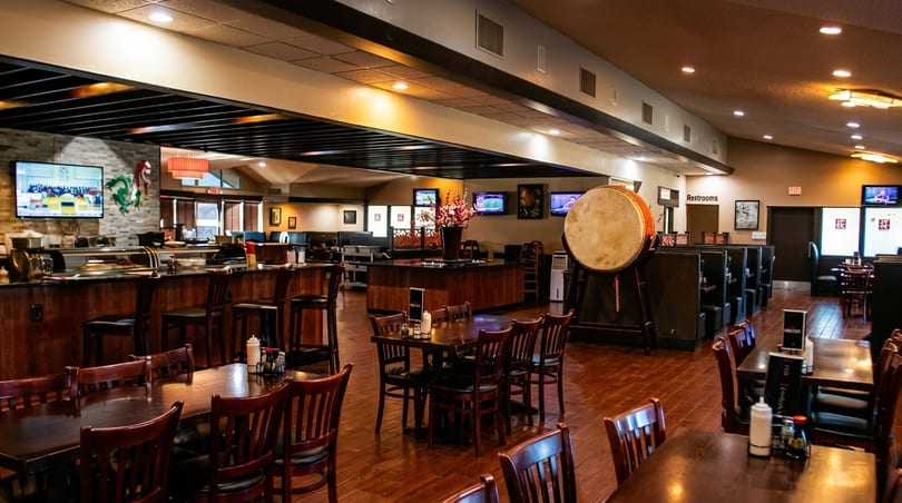 Spacious restaurant interior with wooden tables, chairs, a sushi bar, and a large drum.