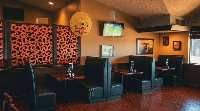 Restaurant interior with black booths, dark wood tables, and decorative orange screens, under warm lighting.
