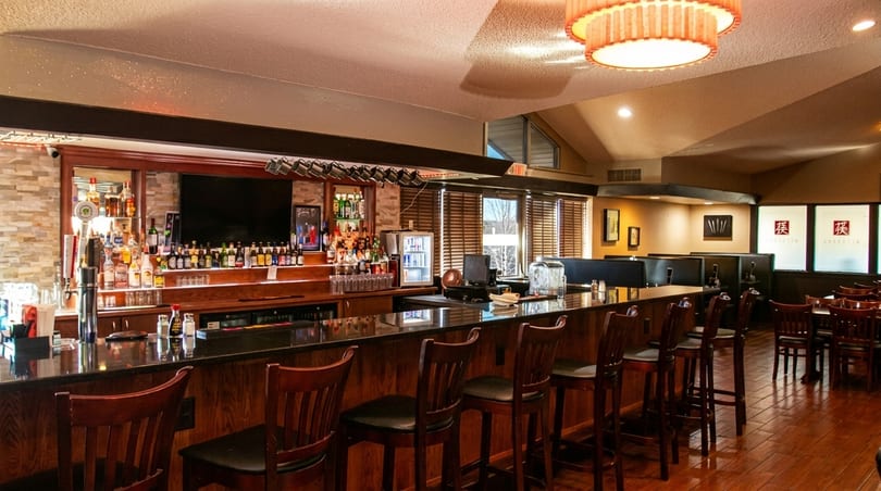 A well-stocked bar with dark wood and granite countertops, surrounded by bar stools and dining tables.