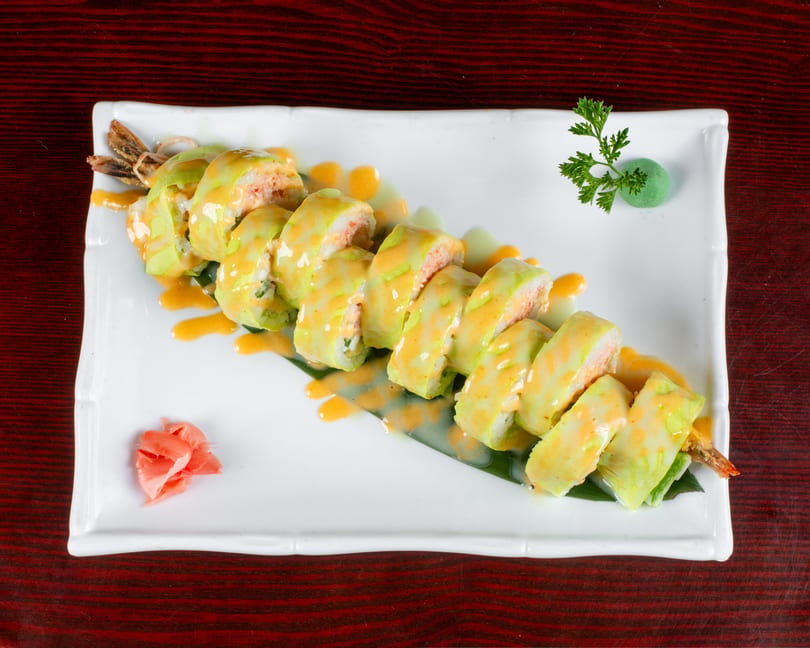 Sushi rolls with light green and orange sauce, garnished with pickled ginger and wasabi.